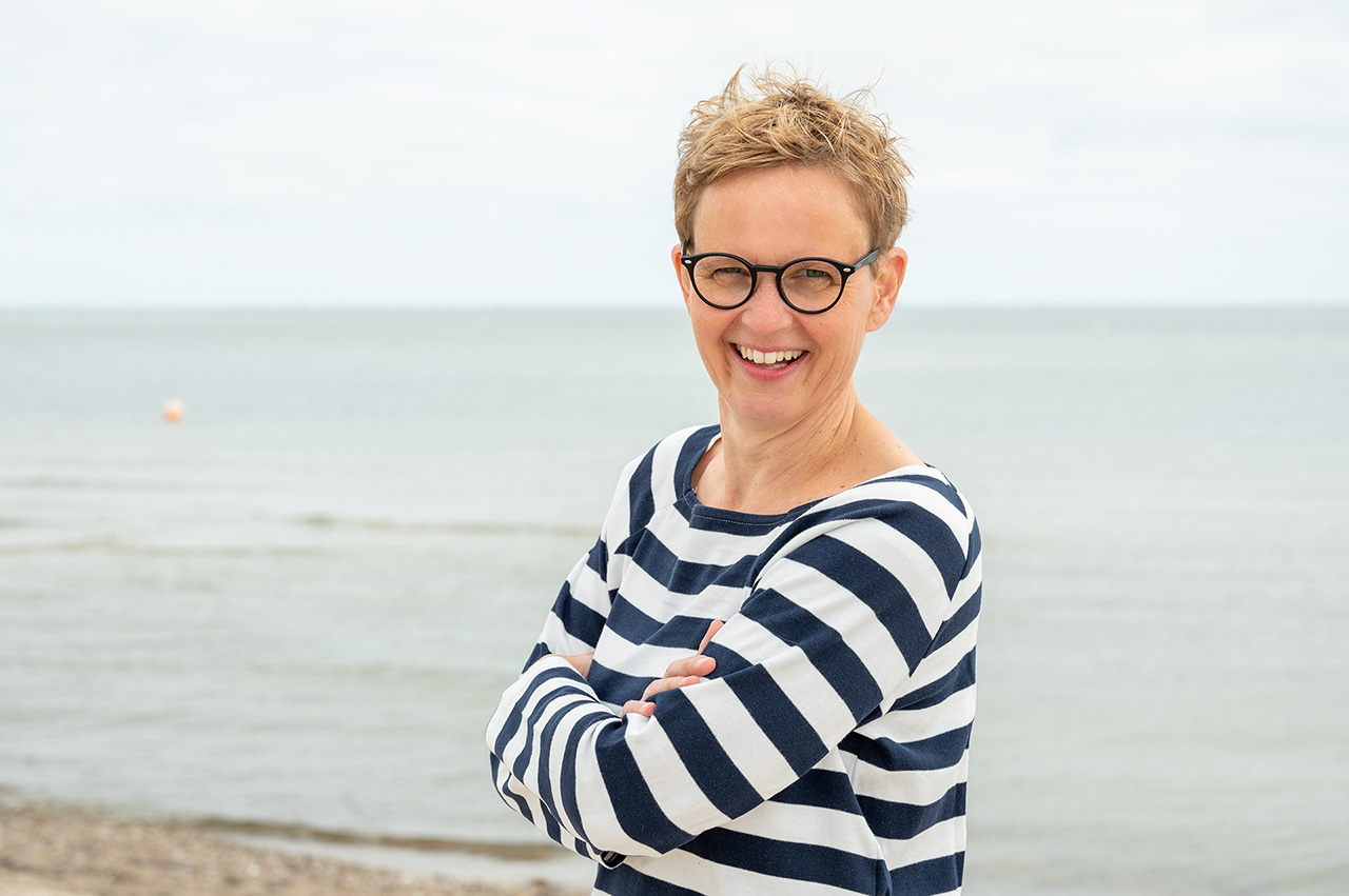 Symbolisch für Ayurveda: Marlene Rostig im blau-weiß geringelten Pullover am Ostsee-Strand in Kiel